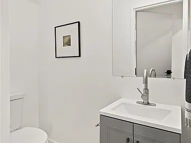 Small, white bathroom with gray vanity, sink, toilet, framed artwork, and medicine cabinet.