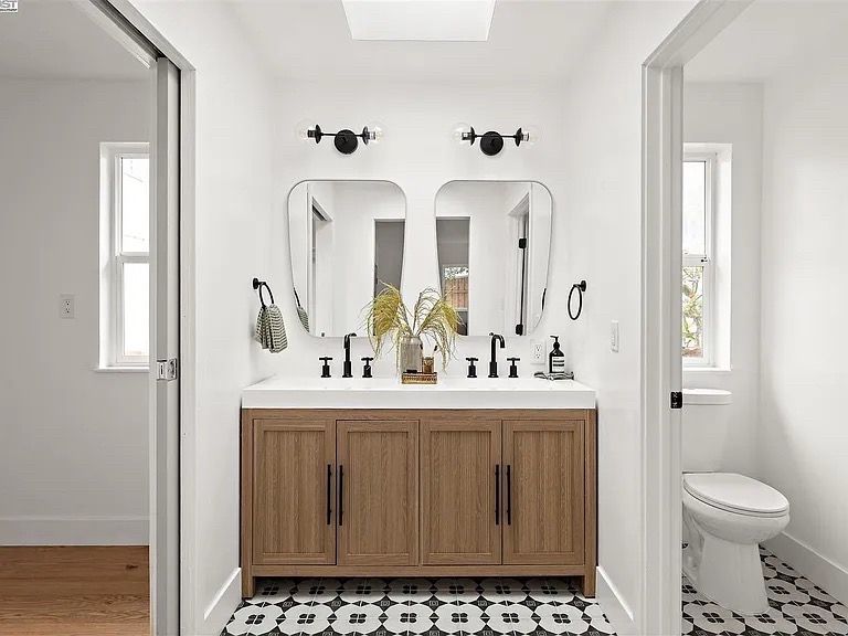 Bathroom with a wooden double vanity, two mirrors, black fixtures, and patterned floor tiles.