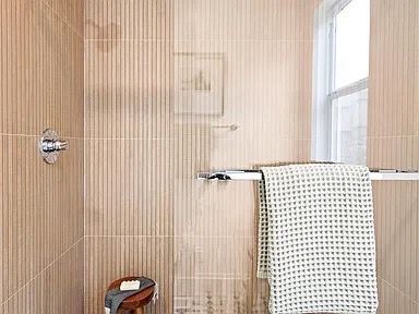 Bathroom interior with beige vertical striped walls, window, towel rack with towel, and wooden stool.