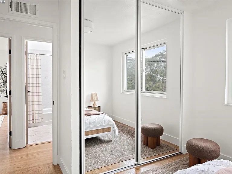 Bedroom with mirrored closet doors; bed, rug, stools, window, and doorway to bathroom.
