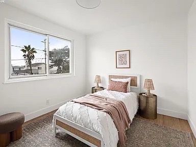 Bedroom with single bed, neutral decor, and large window with palm tree view.