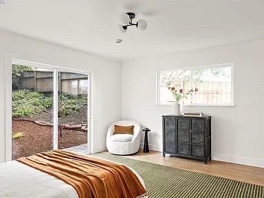 Bedroom with sliding door to a yard, white walls, black cabinet, chair, and a bed with rust-colored blanket.
