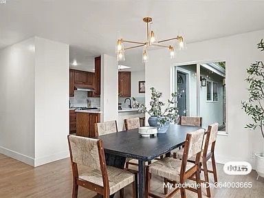 Dining room with dark table, woven chairs, chandelier, and a view into the kitchen.