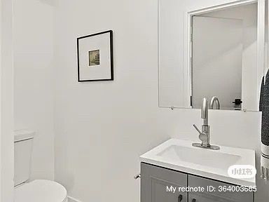 Small, white bathroom with a toilet, sink, mirror, and artwork on the wall.