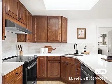 Brown wood kitchen cabinets, white countertops, black appliances, and a skylight.