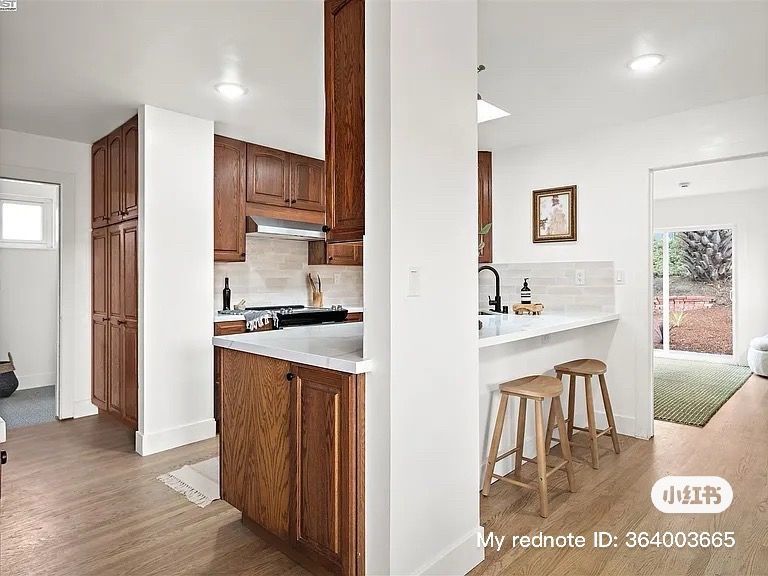 Kitchen with wood cabinets, white countertops, and bar stools.  Doorway to living area with rug.