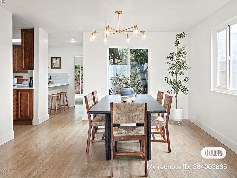 Dining room with dark table, woven chairs, and gold chandelier. Bright, minimalist space with hardwood floors.