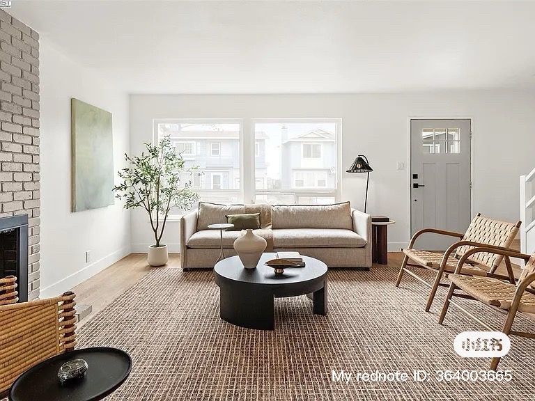 Living room with neutral tones, beige sofa, round black coffee table, brick fireplace, and woven chairs.