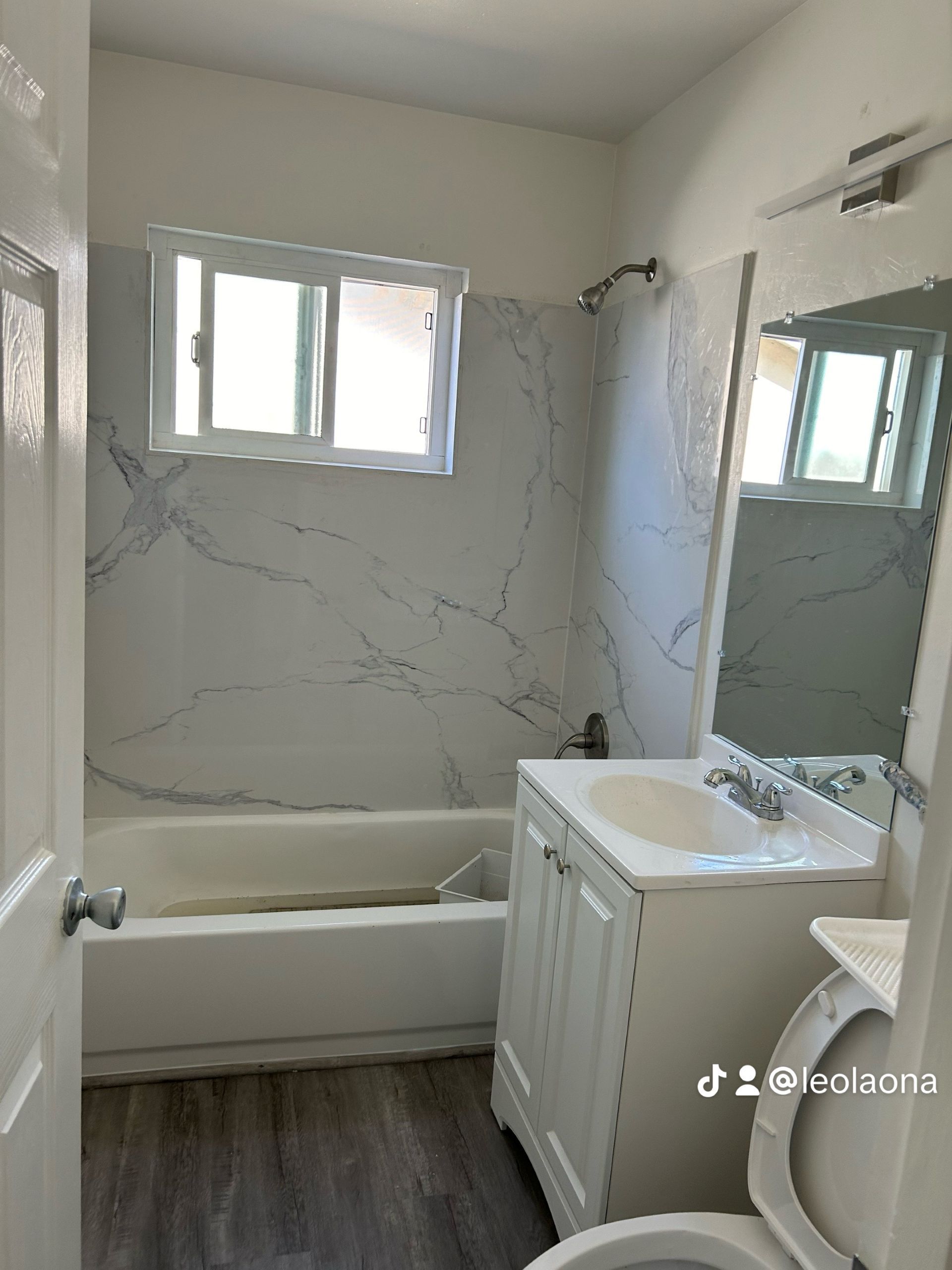 Bathroom with white vanity, bathtub, and marble-look wall panels.  A window is above the tub.