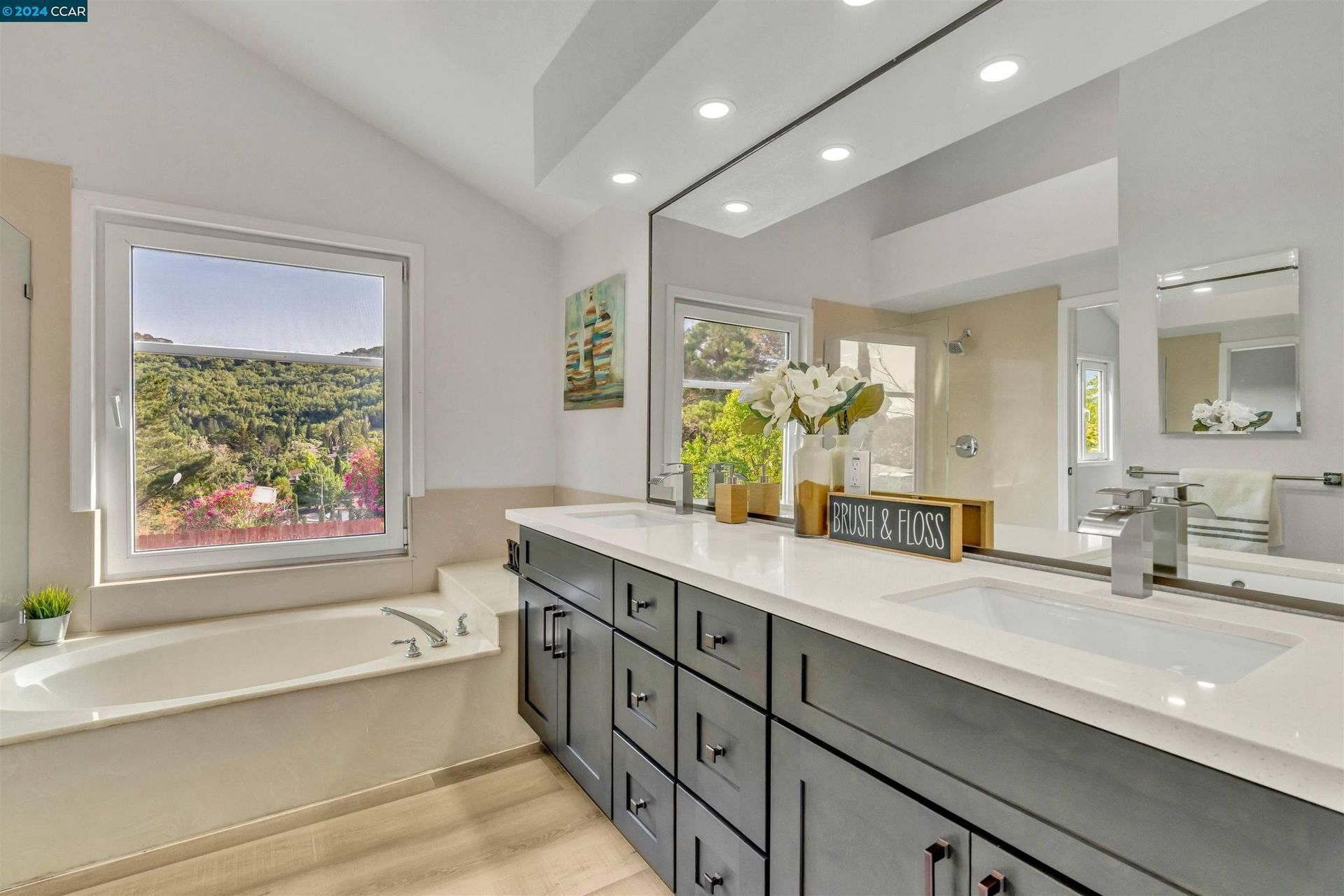 Bathroom with a large vanity and windows overlooking a lush, green landscape; white and gray color scheme.