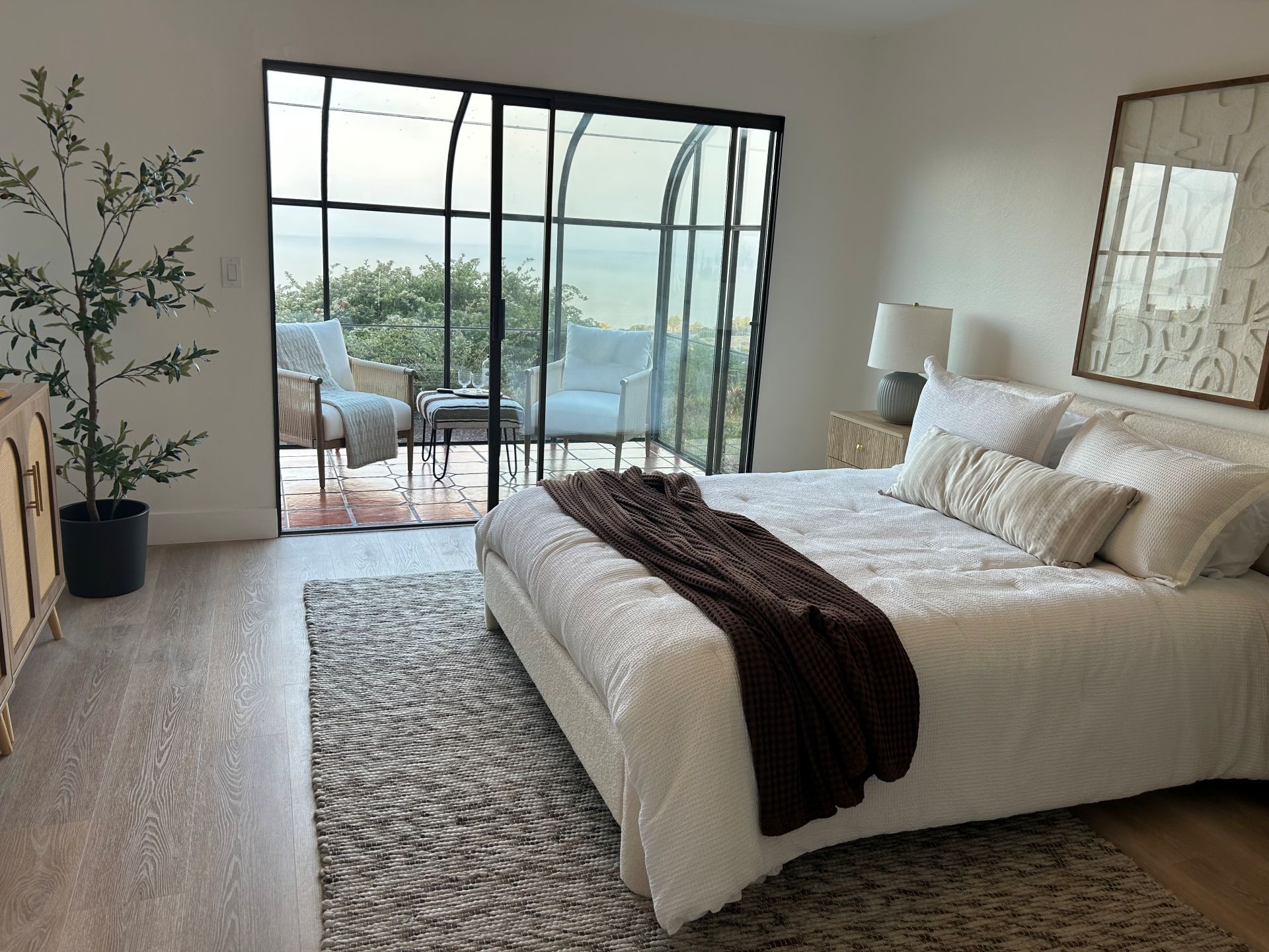 Bedroom with bed, rug, and sliding glass doors to a balcony with chairs and scenic view.