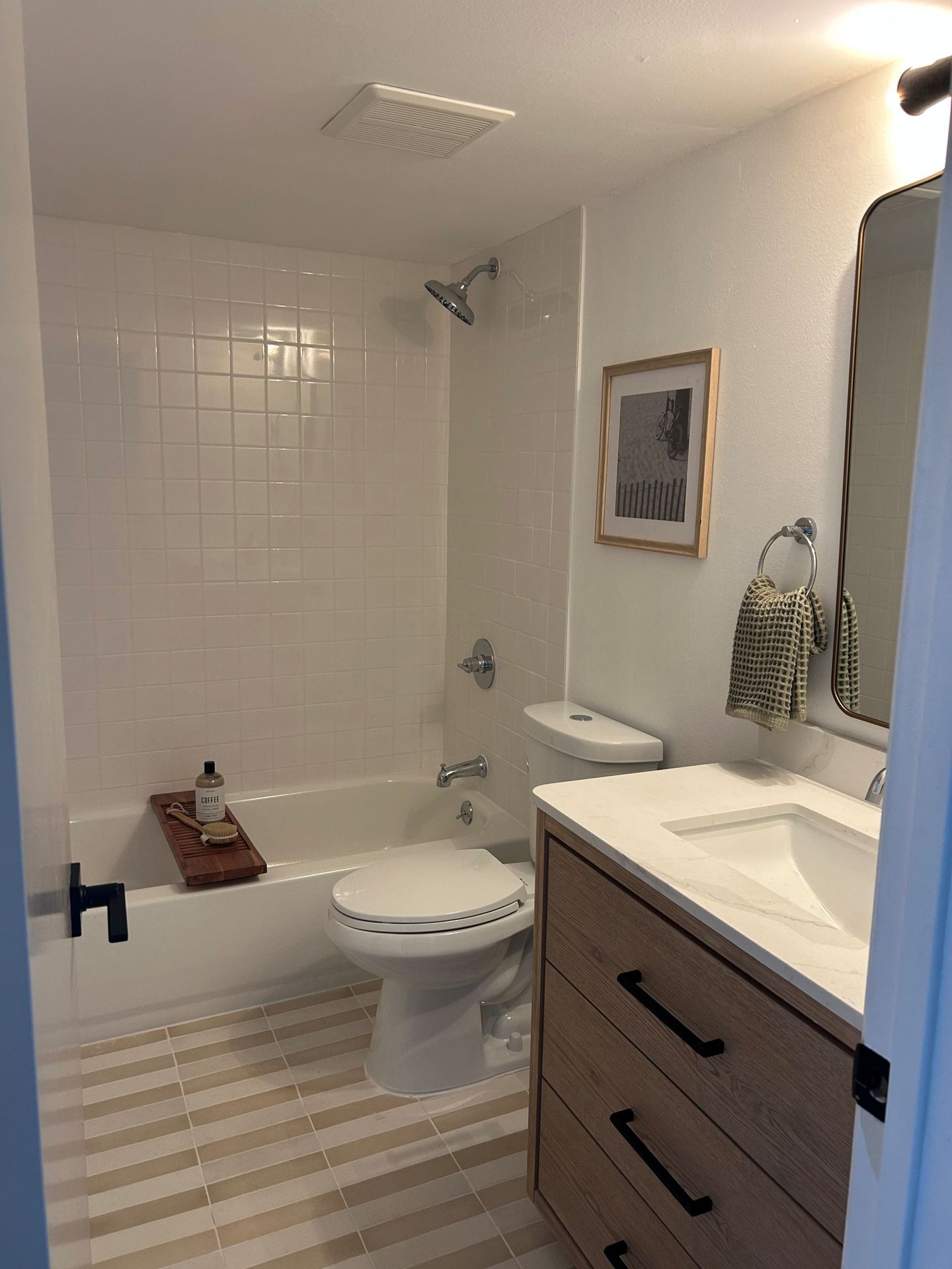 Bathroom with white tile shower, striped floor, wooden vanity, and artwork.