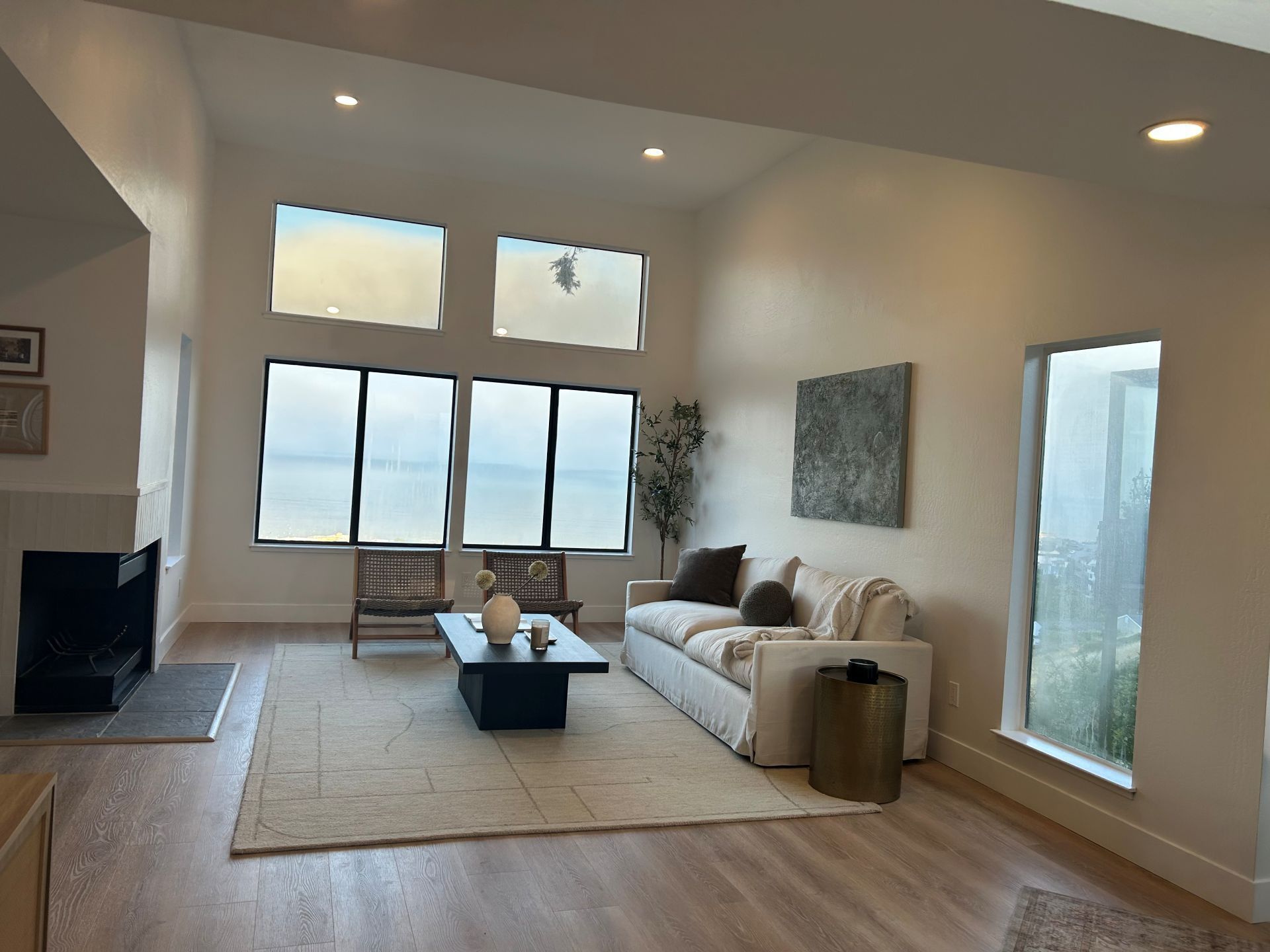 Living room with large windows, fireplace, and neutral-toned furniture.
