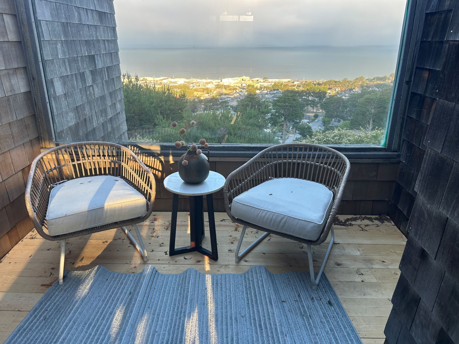 Two wicker chairs with white cushions and a small table on a deck overlooking a body of water.