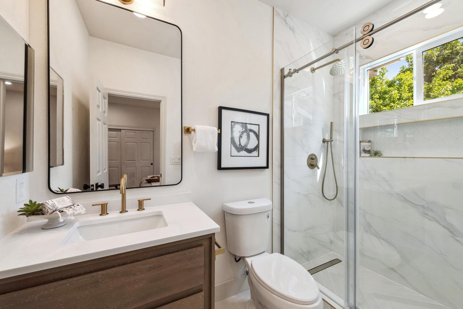 Modern bathroom with white walls, glass shower, and wood vanity with gold fixtures.