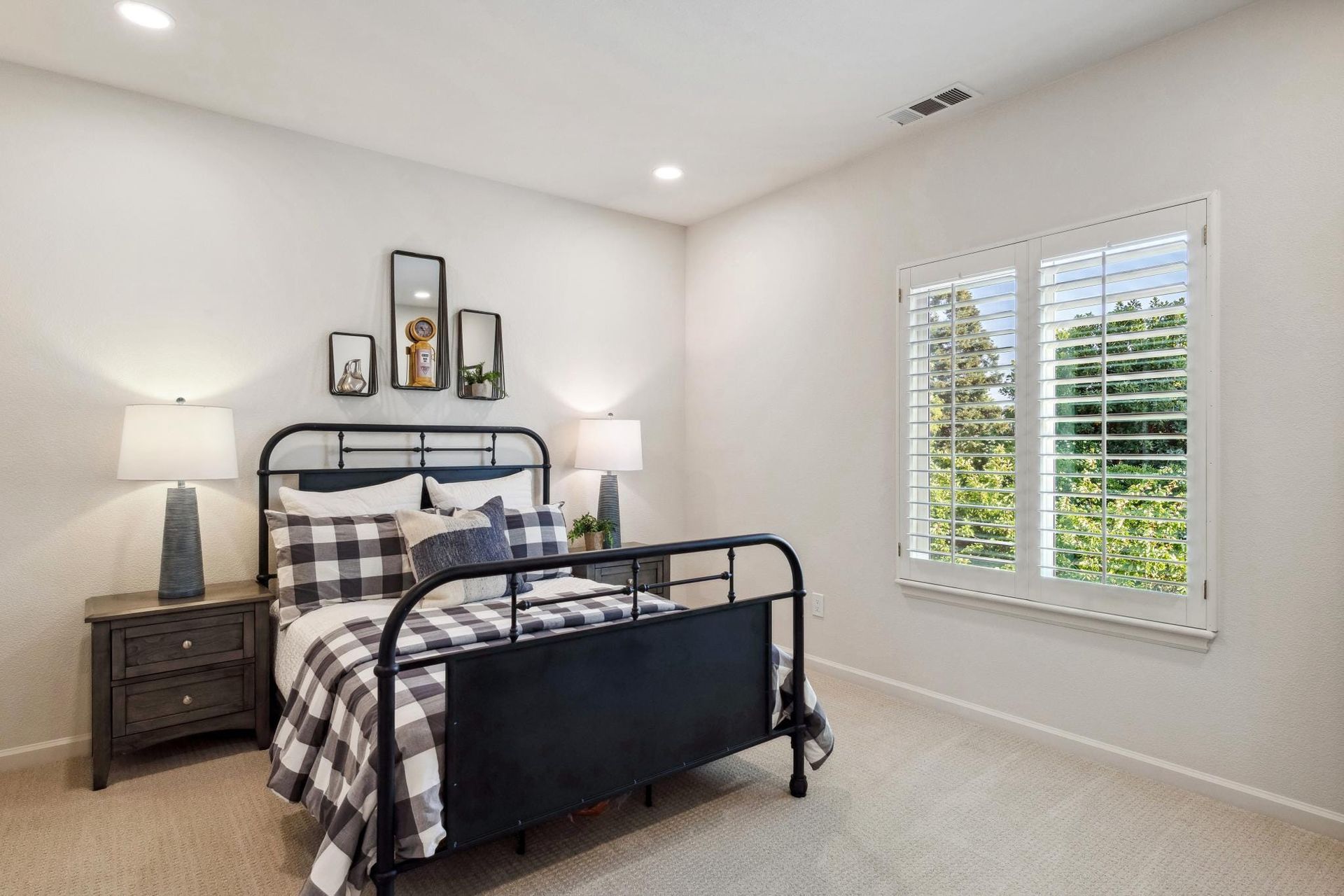 Bedroom with black metal bed, bedside tables, and window with shutters.
