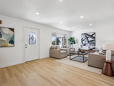 Living room with white walls, light wood flooring, and neutral furniture.
