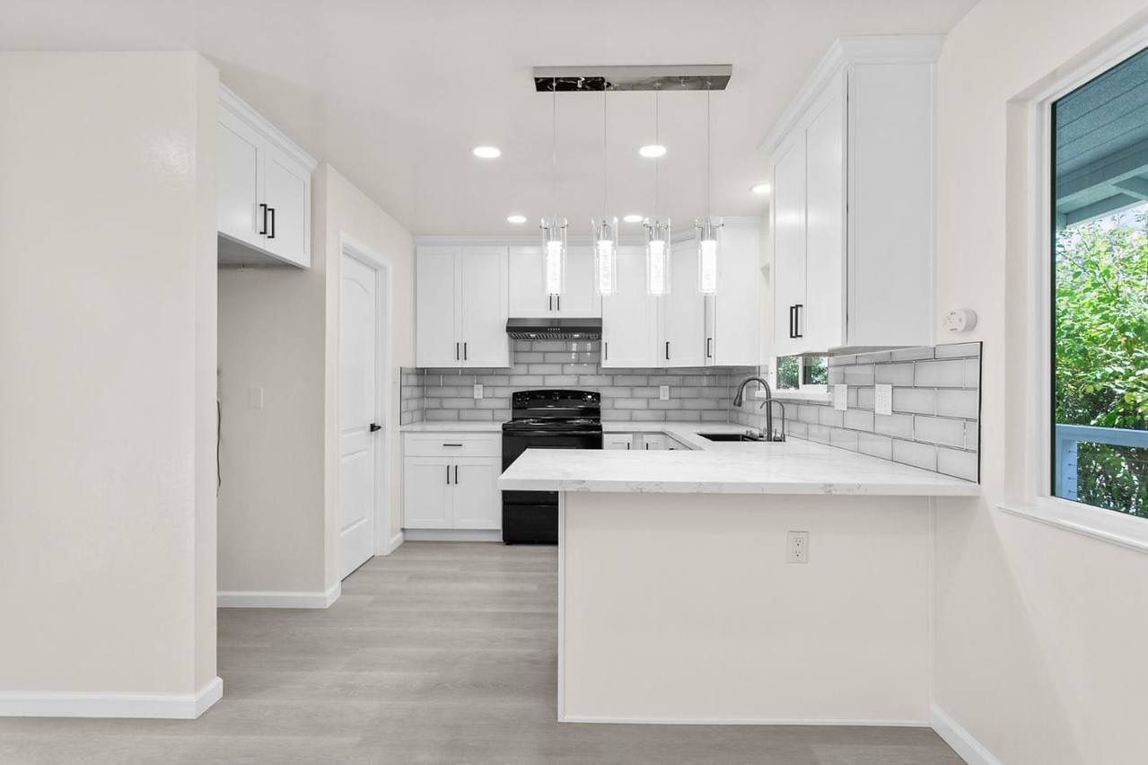 White kitchen with cabinets, gray backsplash, black stove, and counter with view from a window.