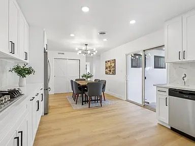 Bright, white kitchen with dining area; cabinets, appliances, table, chairs, and sliding glass door.