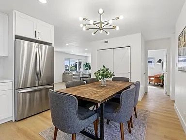Dining area with wooden table, gray chairs, stainless steel refrigerator, and modern chandelier.
