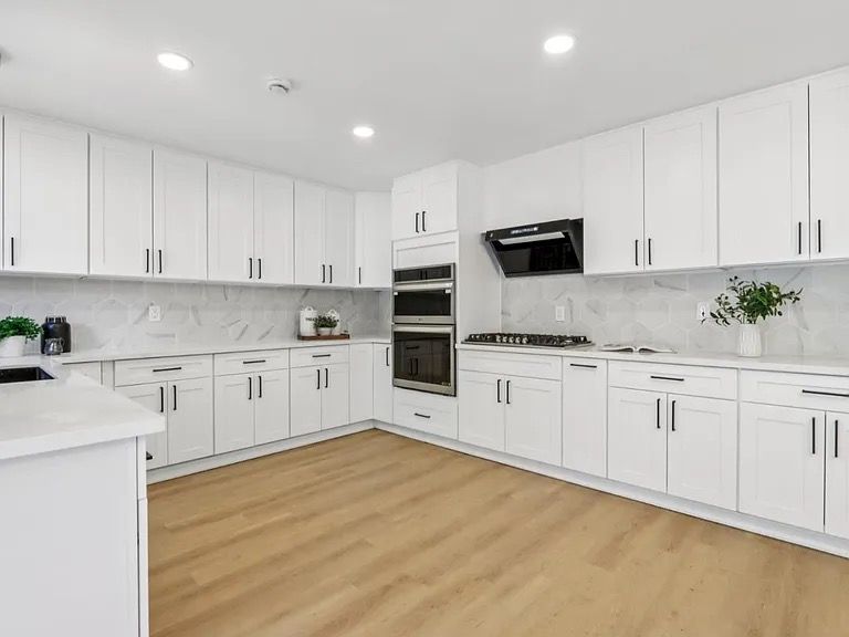 Modern white kitchen with light wood floors, marble backsplash, and black appliances.