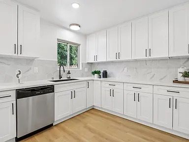 White kitchen with white cabinets, stainless steel appliances, and light wood floors.