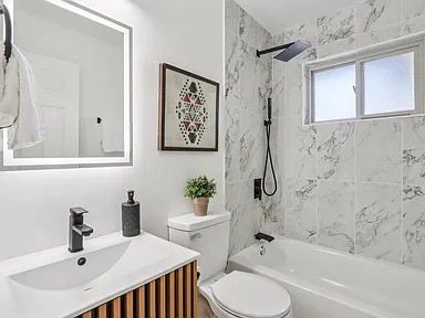Modern bathroom with white marble tile, black fixtures, and a framed artwork.