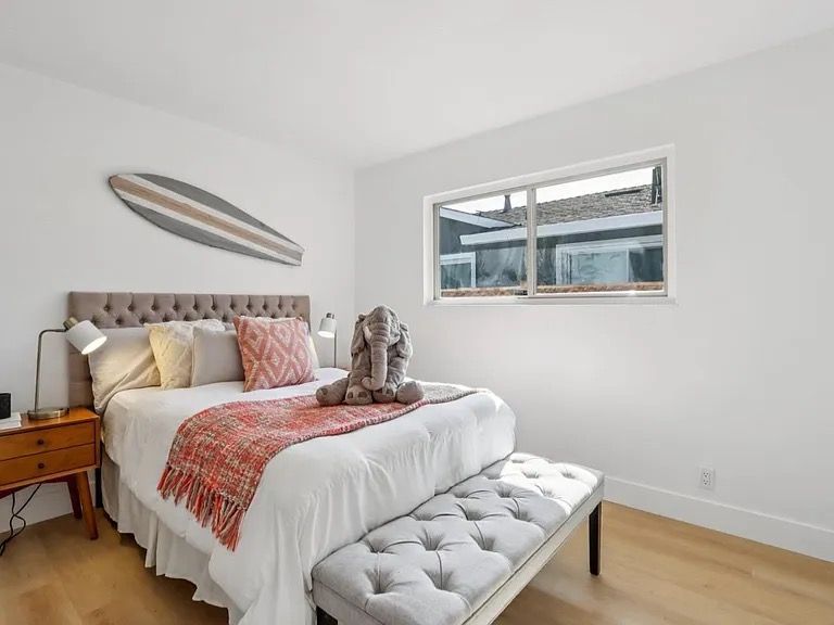 Bedroom with a tufted headboard, a bench, a surfboard, and a window overlooking a home.