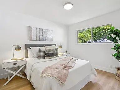 Bedroom with white walls, bed, nightstands, and a large window overlooking greenery.