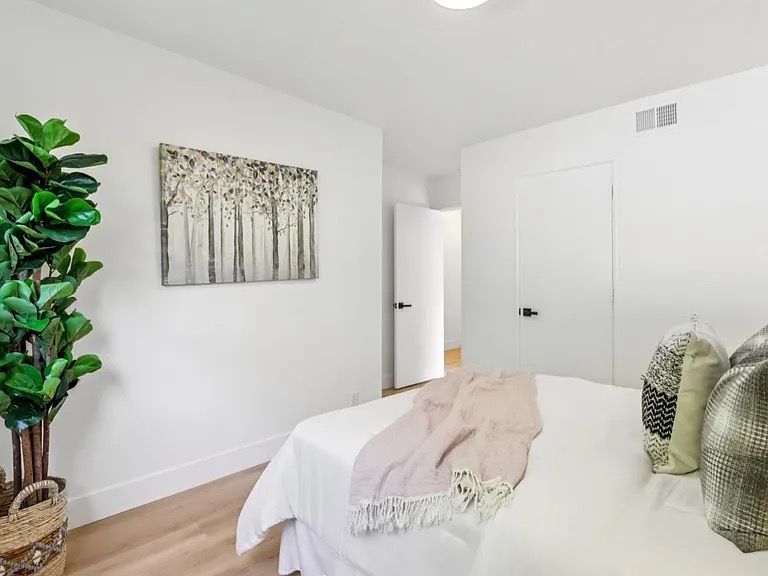Bedroom with white walls, bed, art, and a large plant in a woven basket.