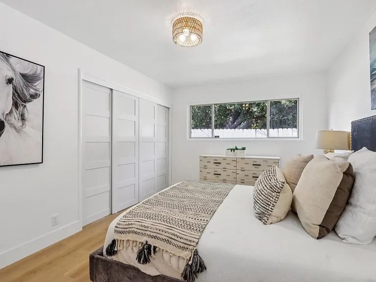 Bedroom with white walls, sliding doors, bed, and decorative pillows. Window view of trees.