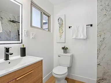Modern white bathroom with wood vanity, black fixtures, and marble accent wall.