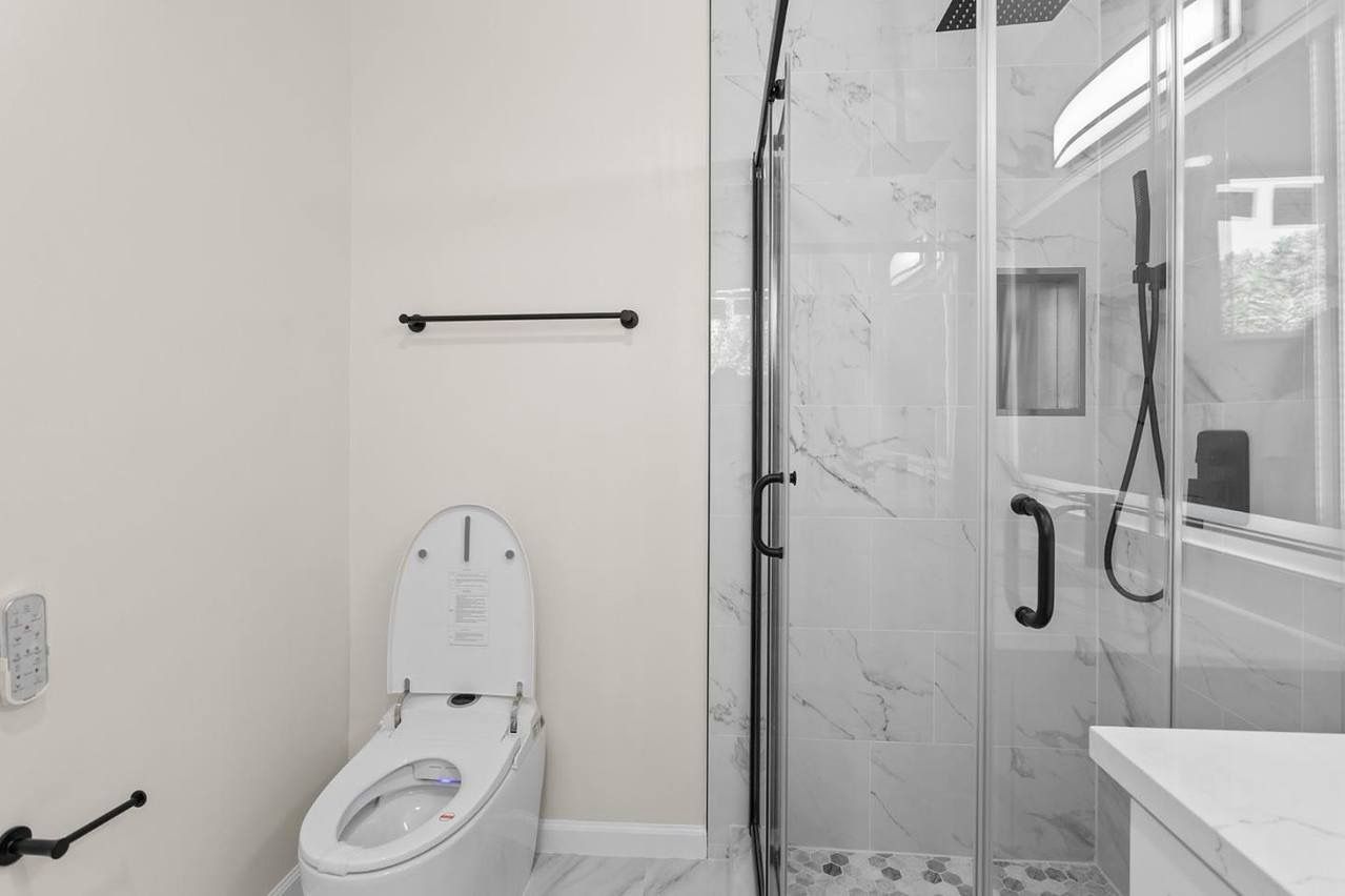 Modern bathroom with a toilet, shower, and towel rack. Black fixtures and white marble tile.