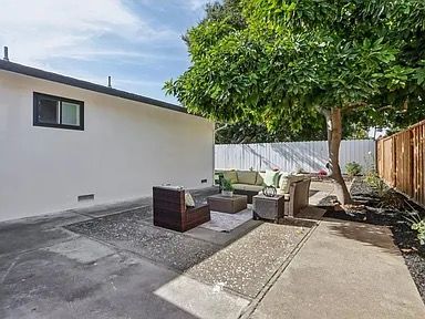 Backyard patio with outdoor furniture beneath a tree and beside a white wall.