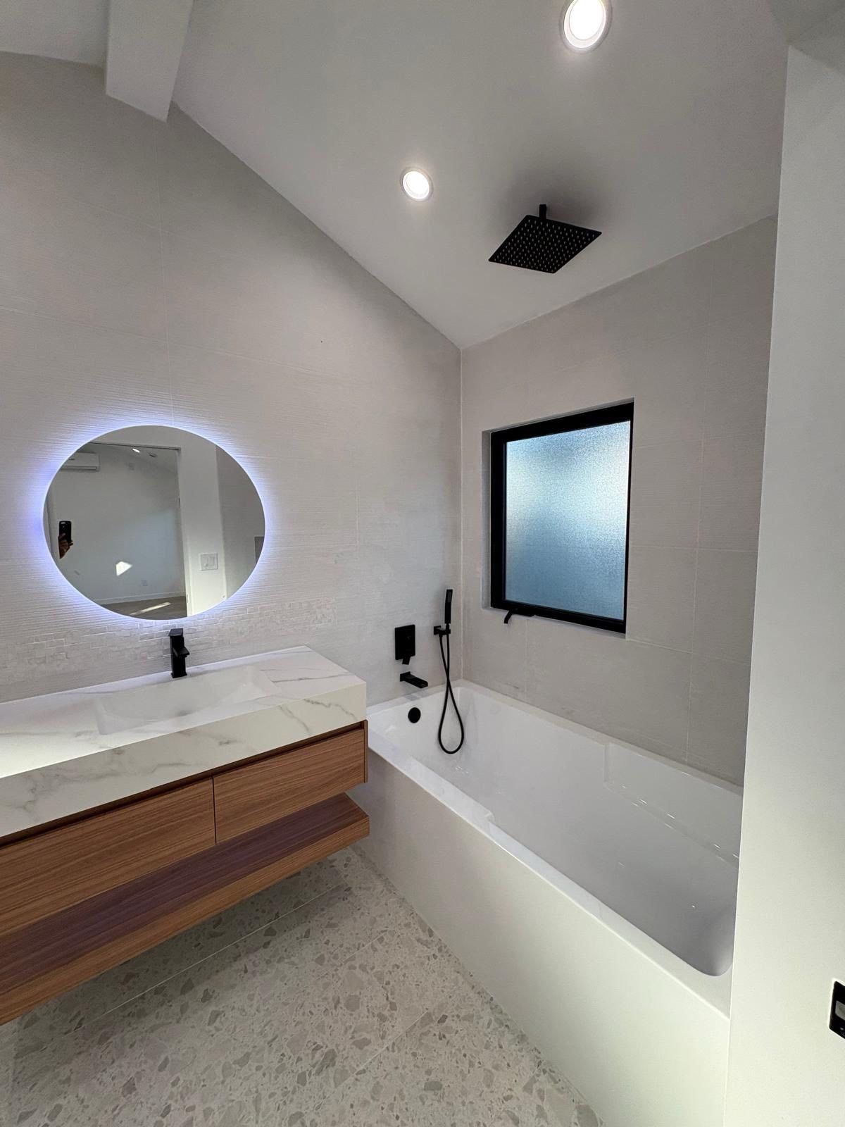 Modern white bathroom with a tub, showerhead, oval mirror, and wooden vanity.