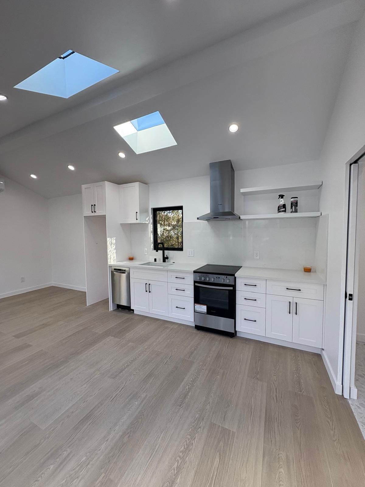 Bright white kitchen with stainless steel appliances, white cabinets, and skylights.