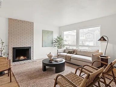 Living room with beige brick fireplace, off-white couch, round black coffee table, wicker chairs, and windows.