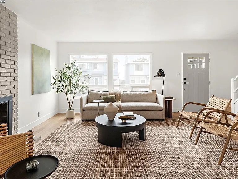 Living room with beige sofa, woven rug, round black coffee table, two chairs, and a fireplace.