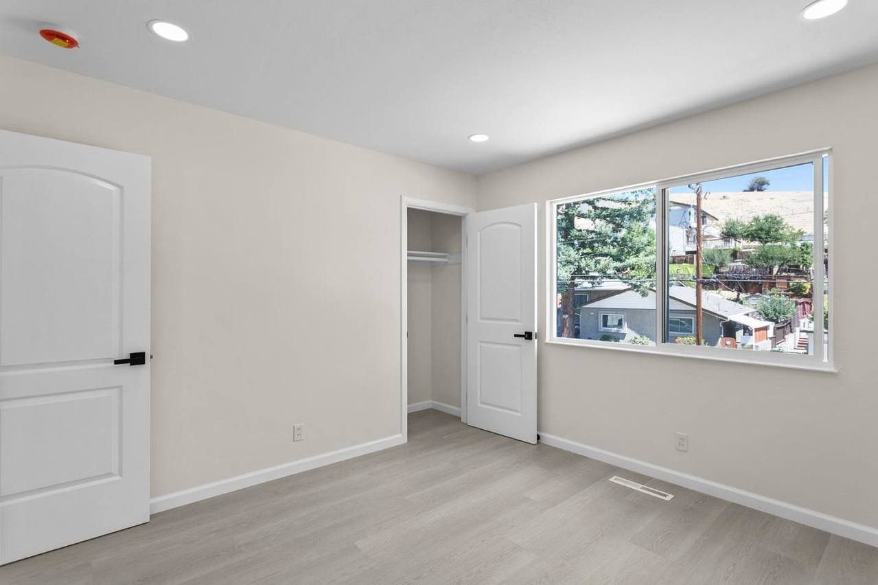 Empty bedroom with white walls, closet, window overlooking trees, and gray carpet.