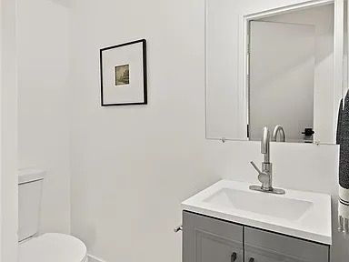 Small, white bathroom with gray vanity, silver faucet, and framed artwork.