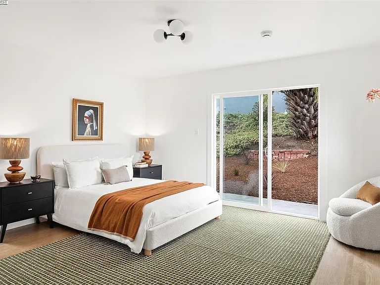 Bedroom with white walls, a bed, black nightstands, a sliding glass door, and a green rug.