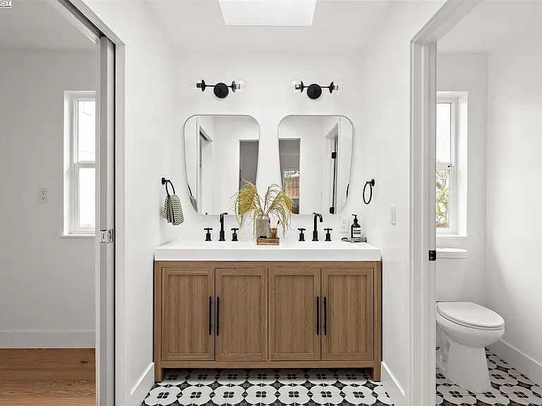 Bathroom with double vanity, wood cabinets, black fixtures, patterned floor, and white walls.