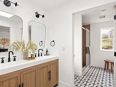Modern bathroom with wood vanity, black fixtures, and patterned tile floor.