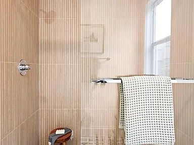 Beige tile bathroom with a towel rack holding a green textured towel and a small wooden stool.
