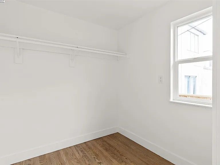 Empty white-walled closet with a hanging rod, a window, and wood-look flooring.