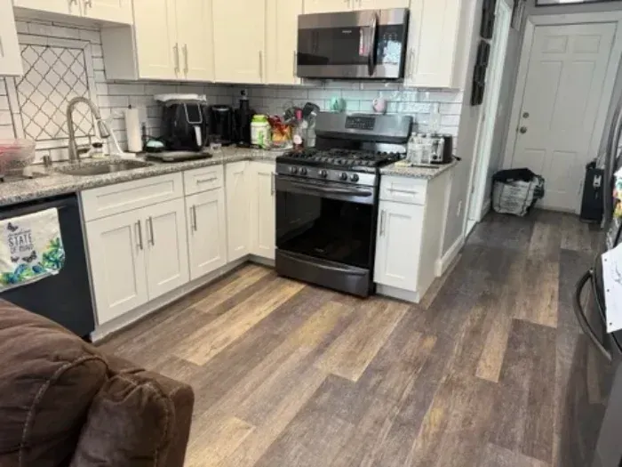 Kitchen with white cabinets, black appliances, and wood-look flooring, viewed from the living room.
