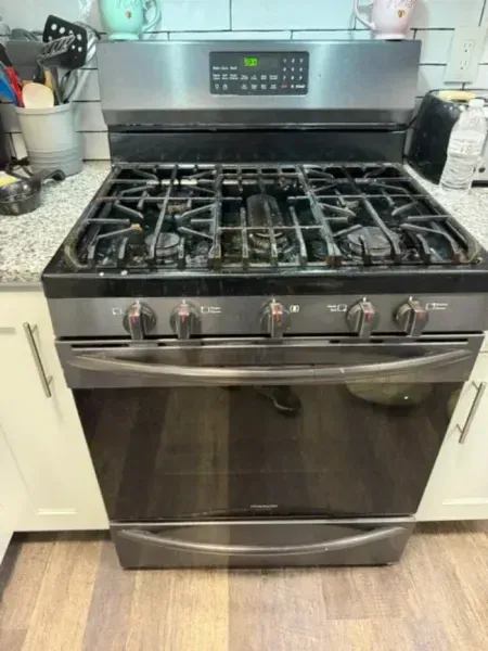 Stainless steel gas range oven in a kitchen with black grates and digital control panel.