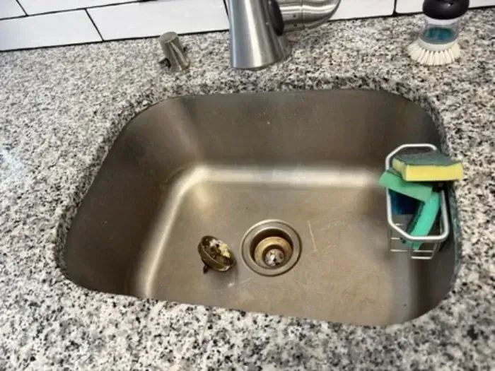 Stainless steel kitchen sink with a sponge and scrub brush in the corner, viewed from above.