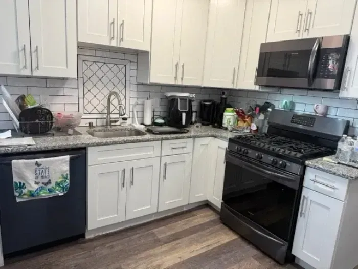 Modern kitchen with white cabinets, black appliances, gray countertops, and wood-look flooring