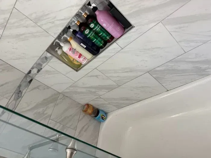 Shower corner with a wall shelf holding shampoo and body wash bottles, next to a glass shower panel.